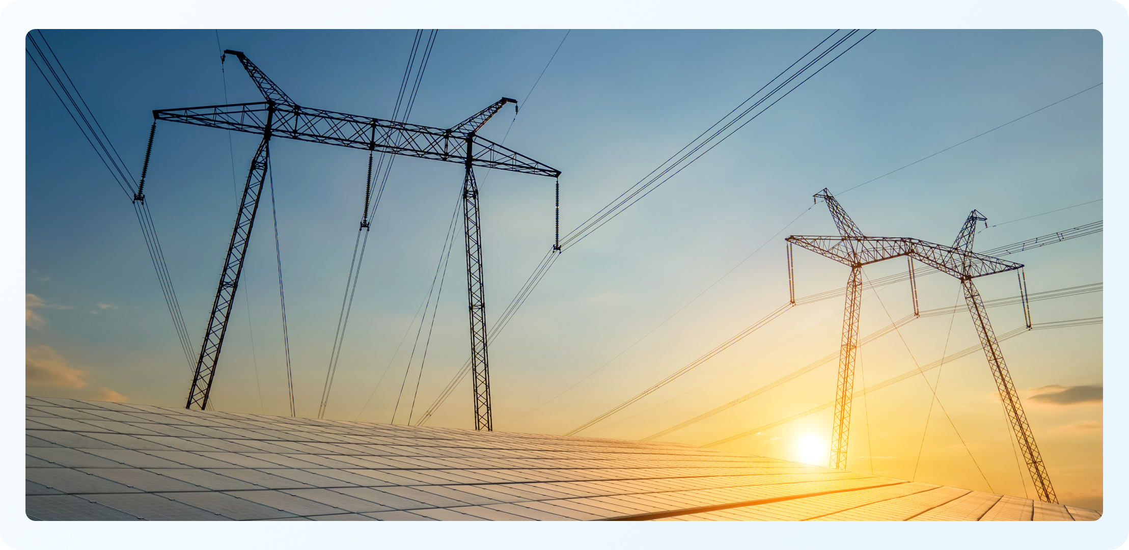 Silhouetted high-voltage transmission towers and power lines above a solar panel field at sunset.