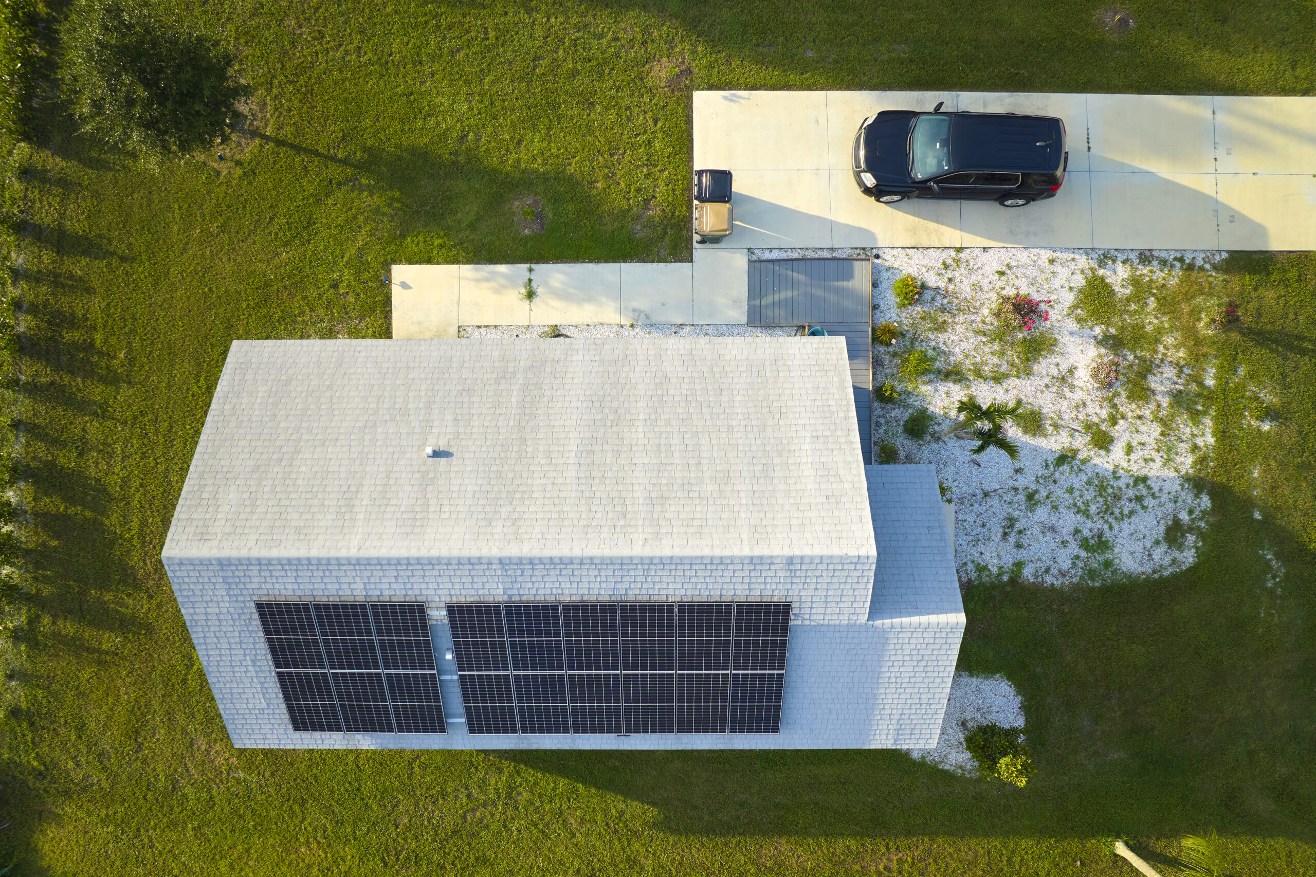 Vue aérienne d'une maison dotée de grands panneaux solaires sur le toit, d'une allée en béton et d'une pelouse verdoyante tout autour.