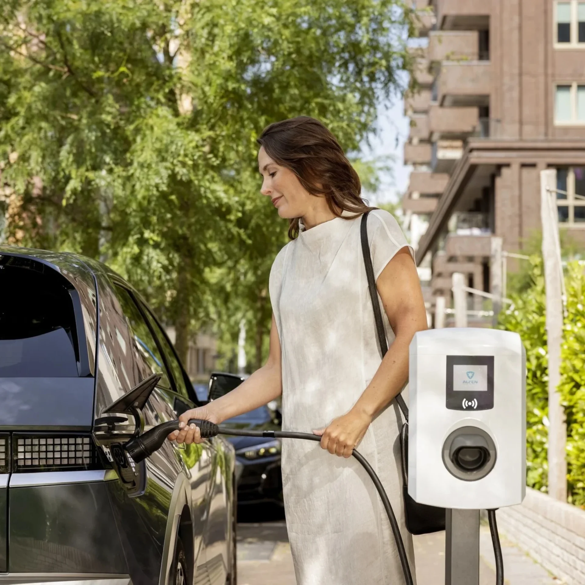 Woman charging an electric car at a public EV charger on a city street.