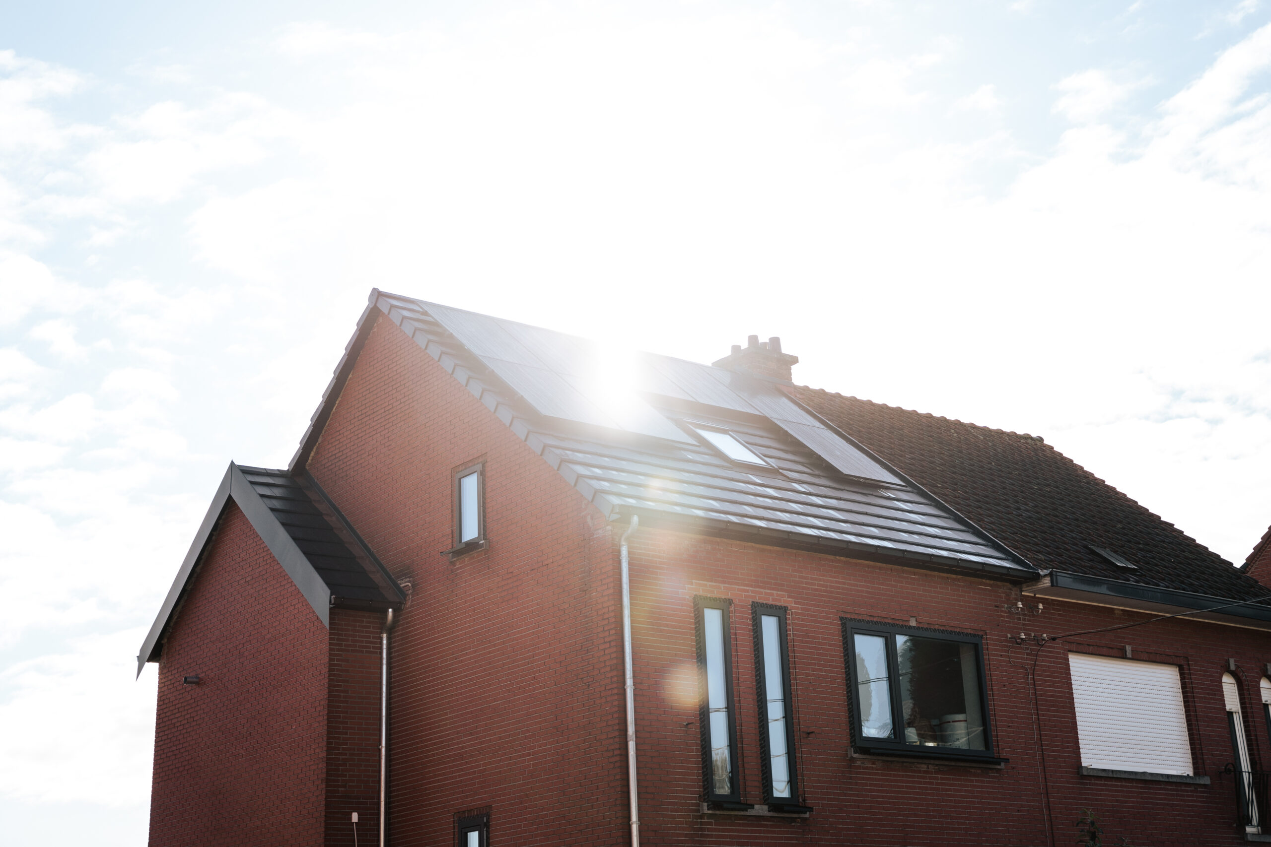 Red brick house with solar panels on the sloped roof under a bright sky.